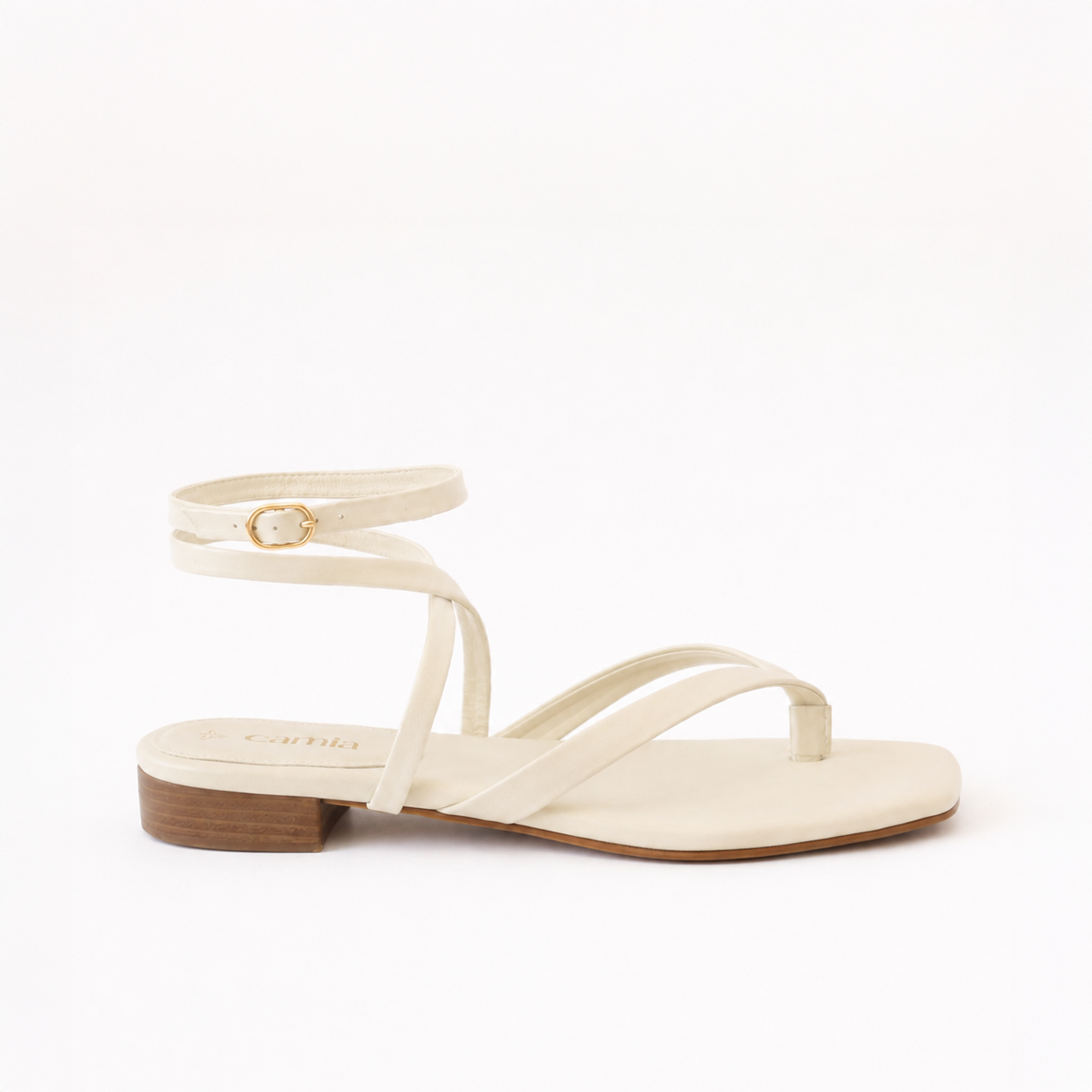 A single flat sandal in a light cream or off-white color, featuring a low block heel, a thong-style toe strap, and an ankle strap with a small gold buckle.